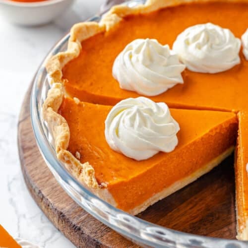 Pumpkin pie in a glass dish with whipped cream dollops on top.