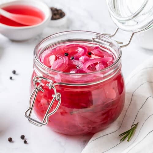 Pickled onion with pickling liquid in a glass jar with ingredients on the side.