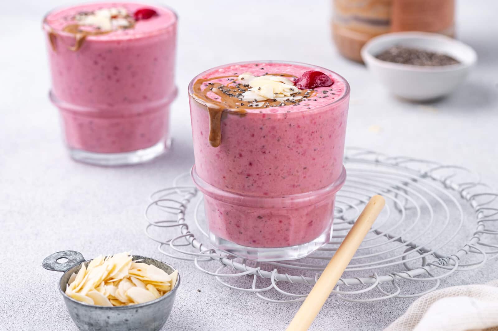 Two glasses filled with a cherry smoothie, topped with almond butter and almonds.