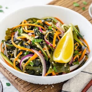 A white bowl of seaweed salad with a lemon wedge, served with chopsticks.