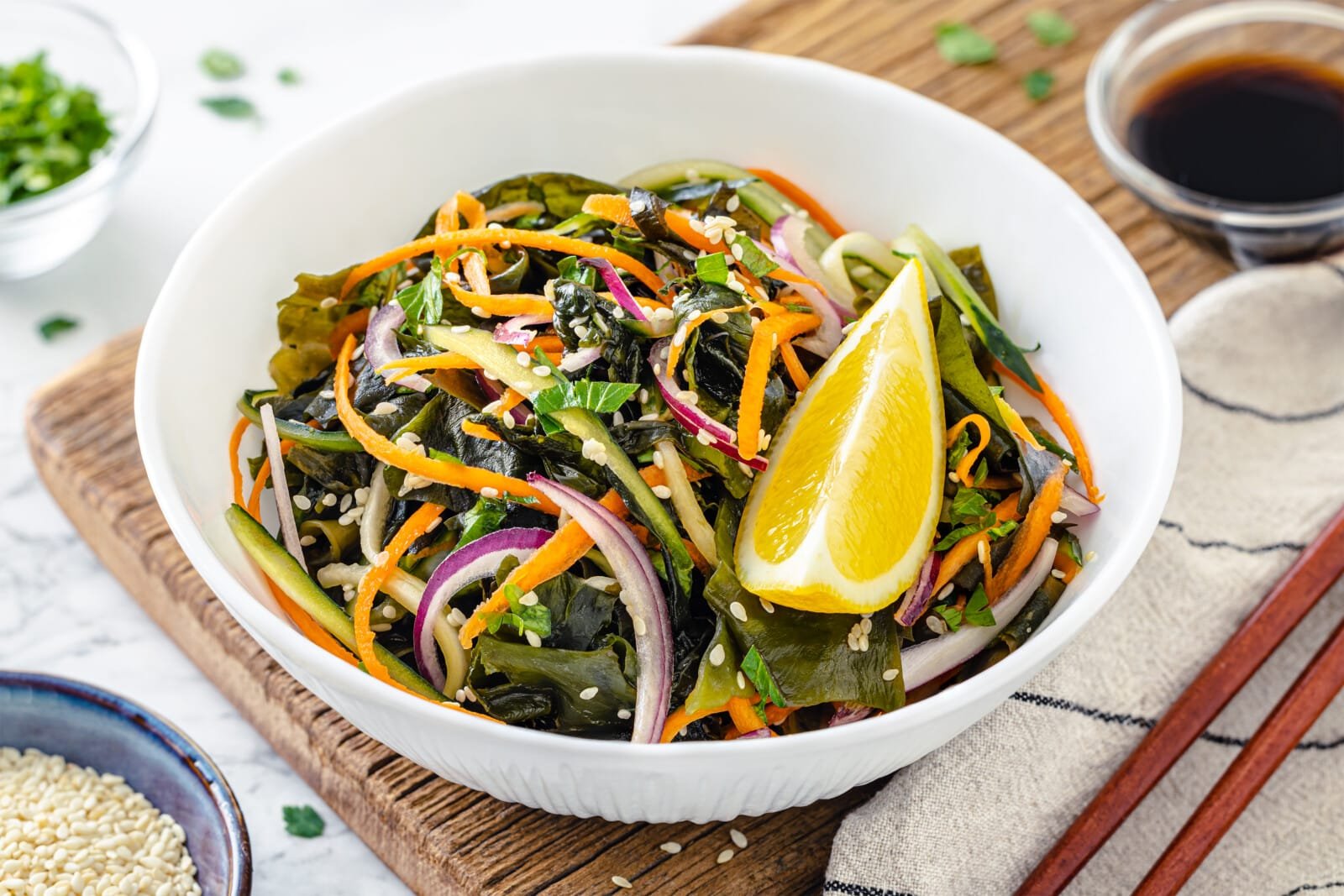 A white bowl of seaweed salad with a lemon wedge, served with chopsticks.