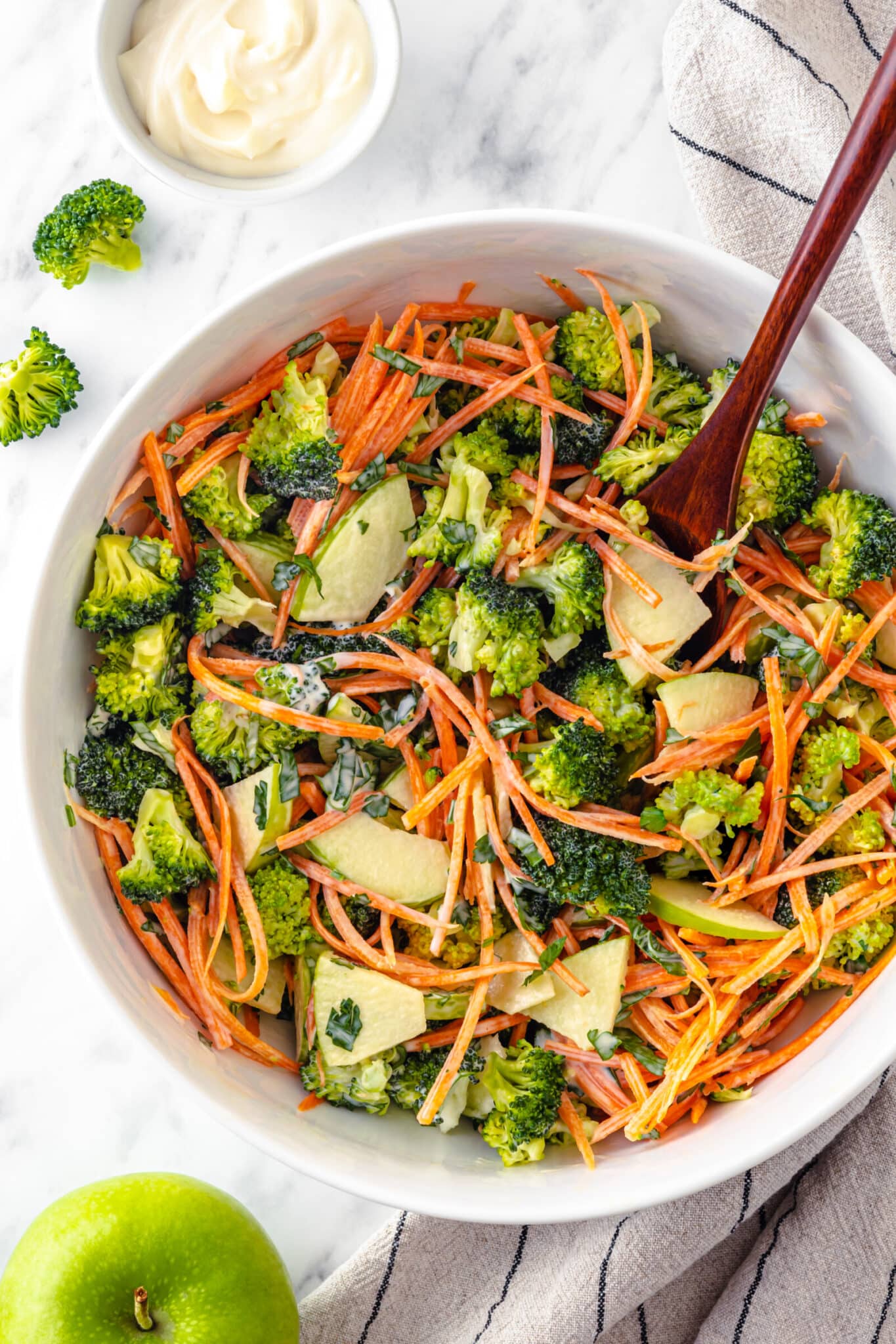 Apple and broccoli salad mixed in a bowl with a wooden spoon.