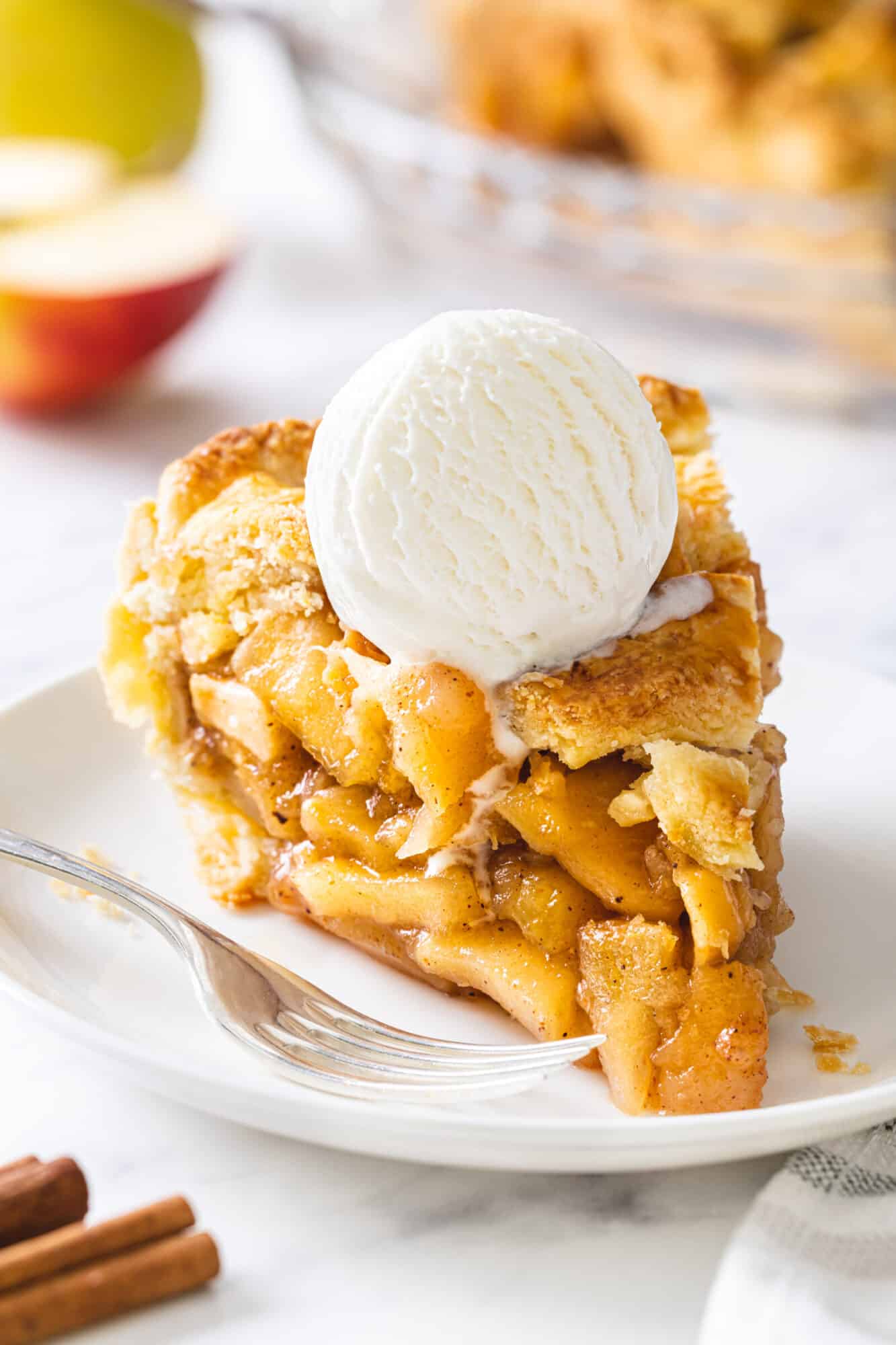 Apple pie with ice cream slice atop a plate with a fork on the side.