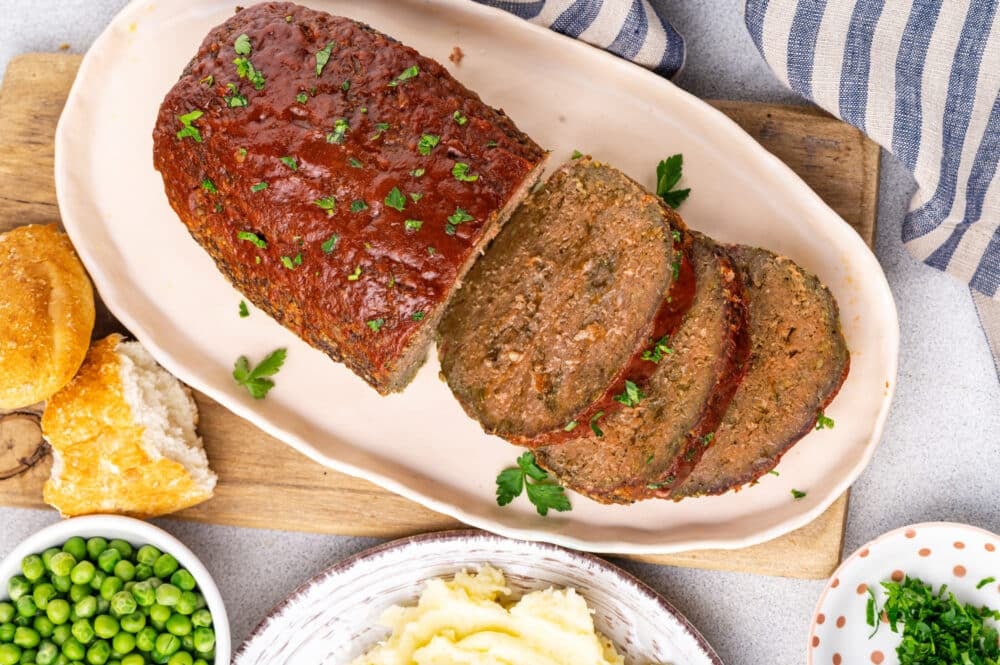 Baked meatloaf sliced and served on an oval plate with parsley garnish.