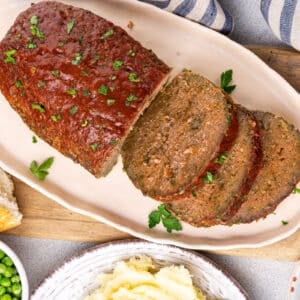 Baked meatloaf sliced and served on an oval plate with parsley garnish.