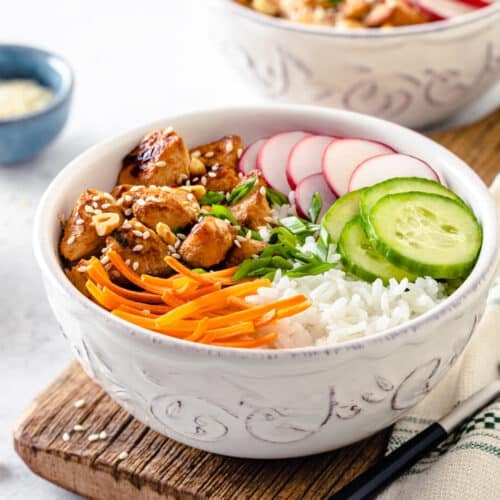 Chicken atop a rice bowl with sliced veggies, served with a fork on the side.