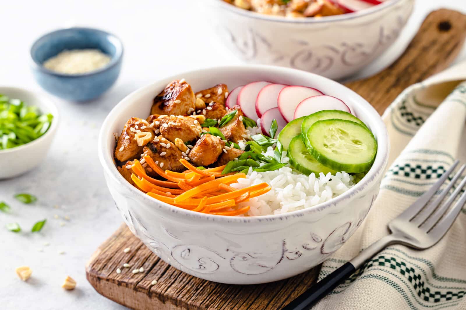 Chicken atop a rice bowl with sliced veggies, served with a fork on the side.
