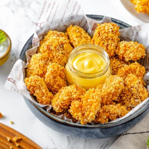 Chicken nuggets in a bowl with dip, ready to eat with more ranch dip on the side.