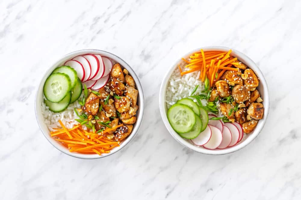 Chicken rice bowl assembled with rice on the bottom, laid out veggies, and chicken on top.