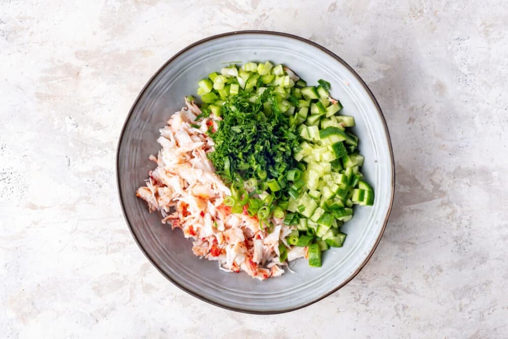Chopped celery, cucumber, parsley, green onion, dill, and crab in a bowl.