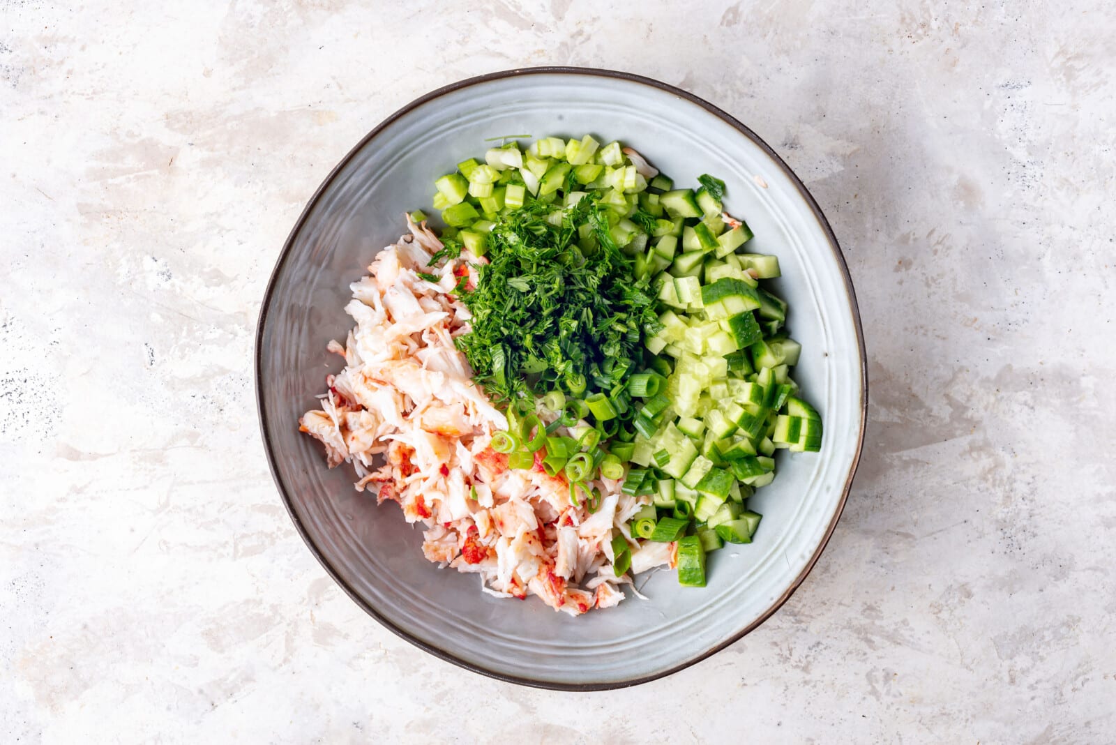 Chopped celery, cucumber, parsley, green onion, dill, and crab in a bowl.