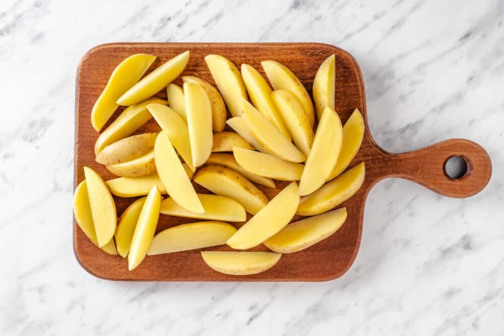 Chopped potato wedges atop a wooden board.