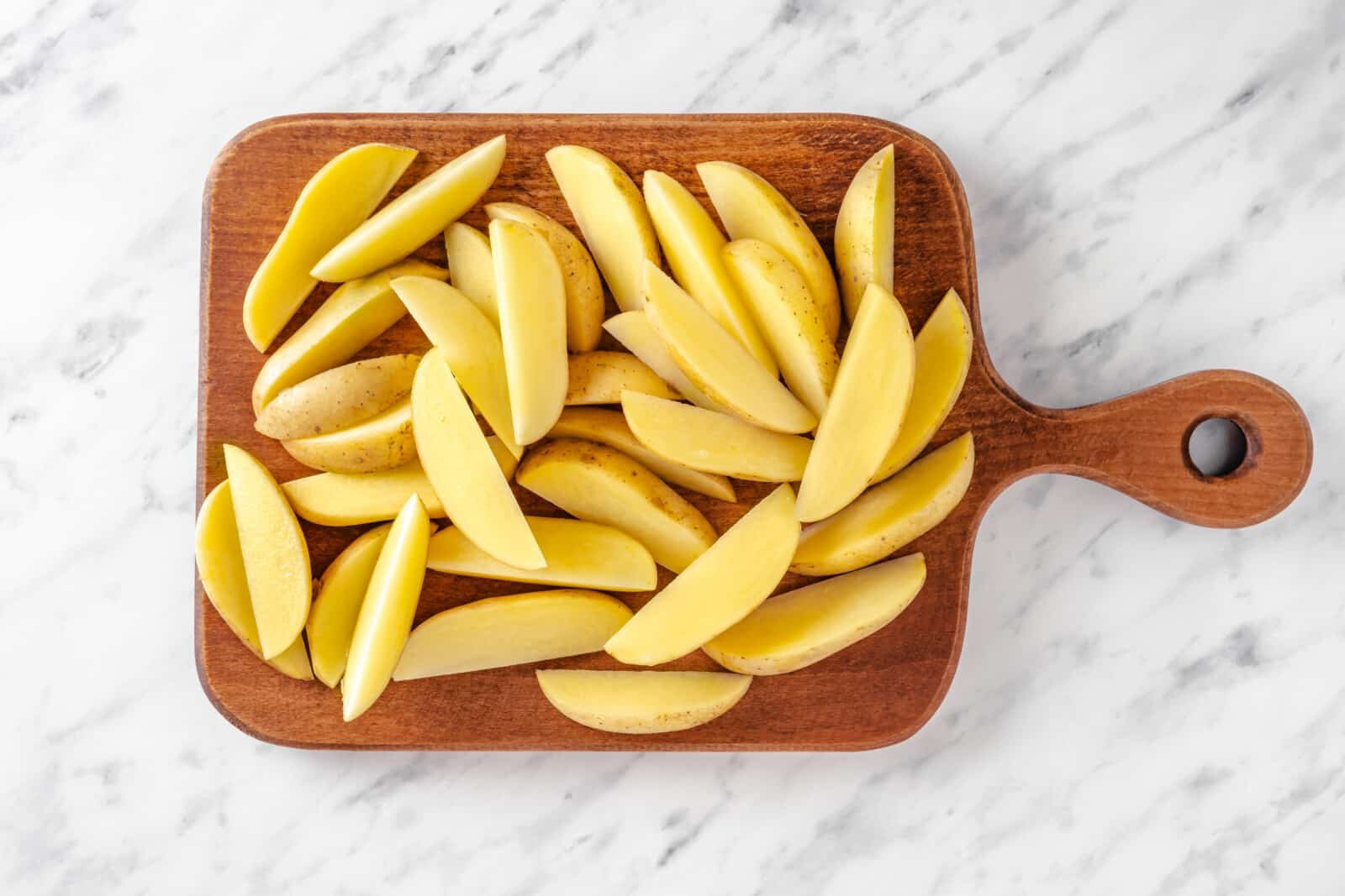 Chopped potato wedges atop a wooden board.