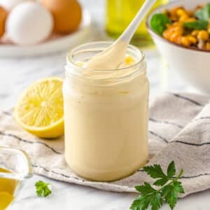 How to Make Mayonnaise From Scratch Delicious creamy mayonnaise in a glass jar, serving with a white spoon.