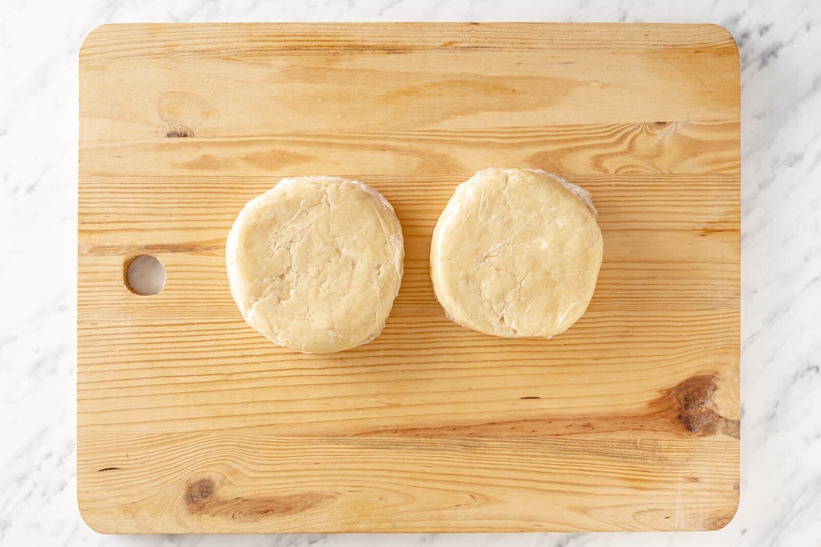 Dough balls wrapped in clear plastic atop a wooden board.