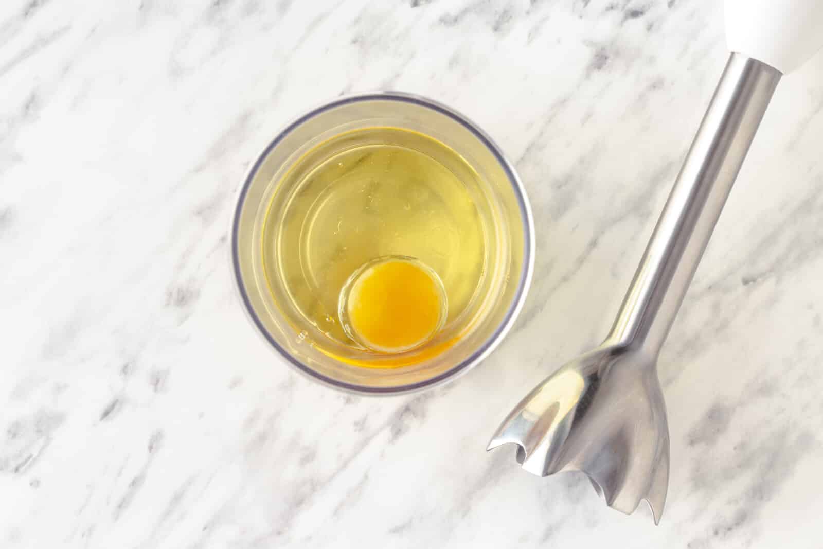 How to Make Mayonnaise From Scratch Egg in a glass with an immersion blender on the side.