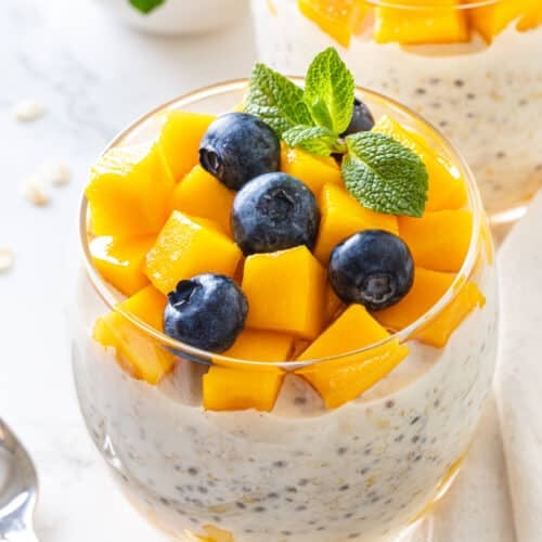Mango Overnight Oats with Blueberries and Mint in a glass.
