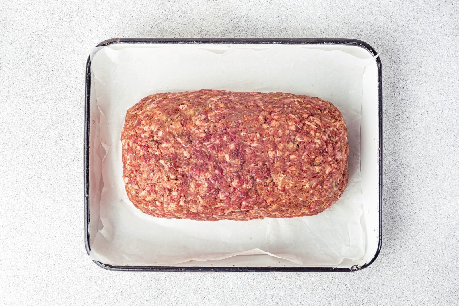 Meatloaf roll in a pan with parchment paper ready to bake.