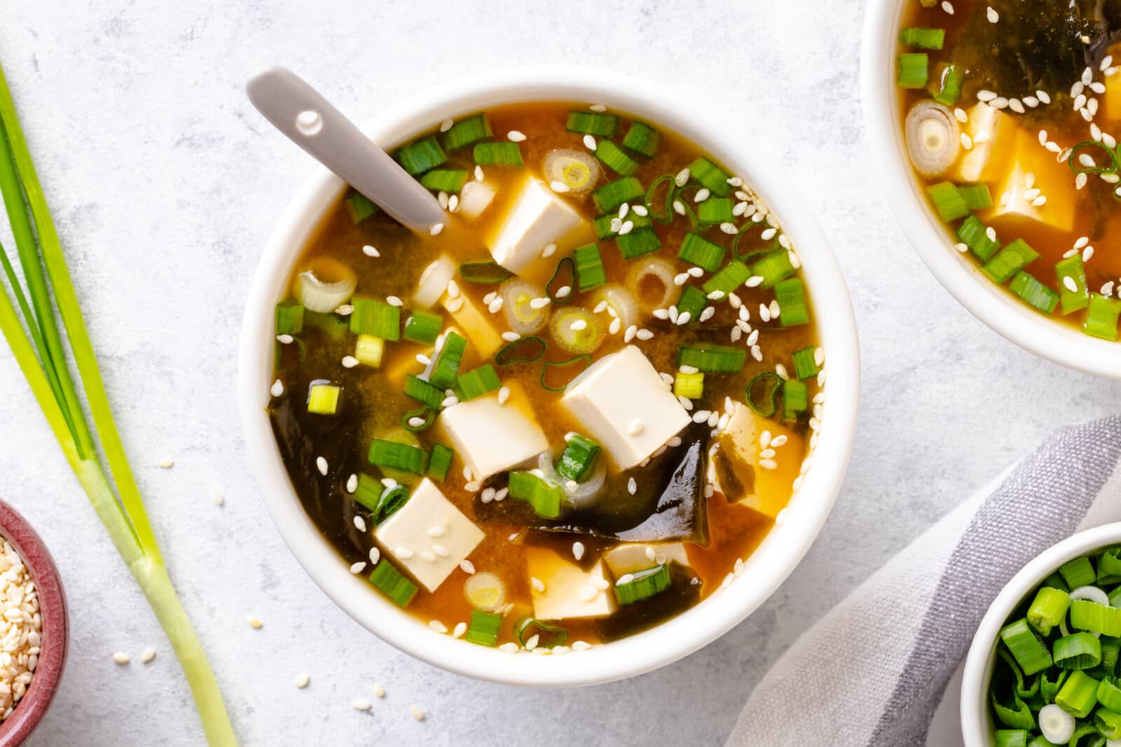 How To Make Miso Soup At Home Miso soup garnished with green onions and sesame seeds in a white bowl with a spoon.