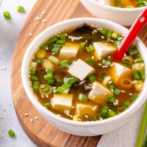 How To Make Miso Soup At Home Miso soup in a large white bowl, serving atop a wooden board with green onion on the side.
