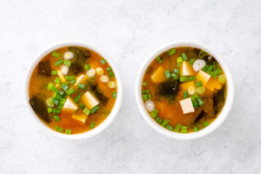 Miso soup in two bowls with chopped green onion on top as garnish.