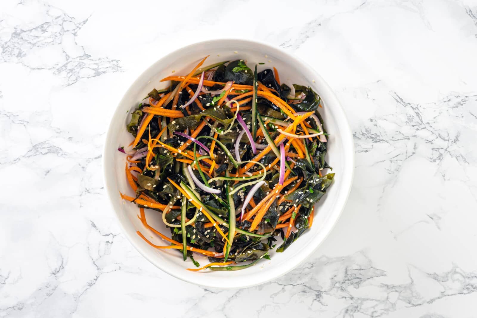 Mixed seaweed salad with dressing and sesame seeds in a white bowl.
