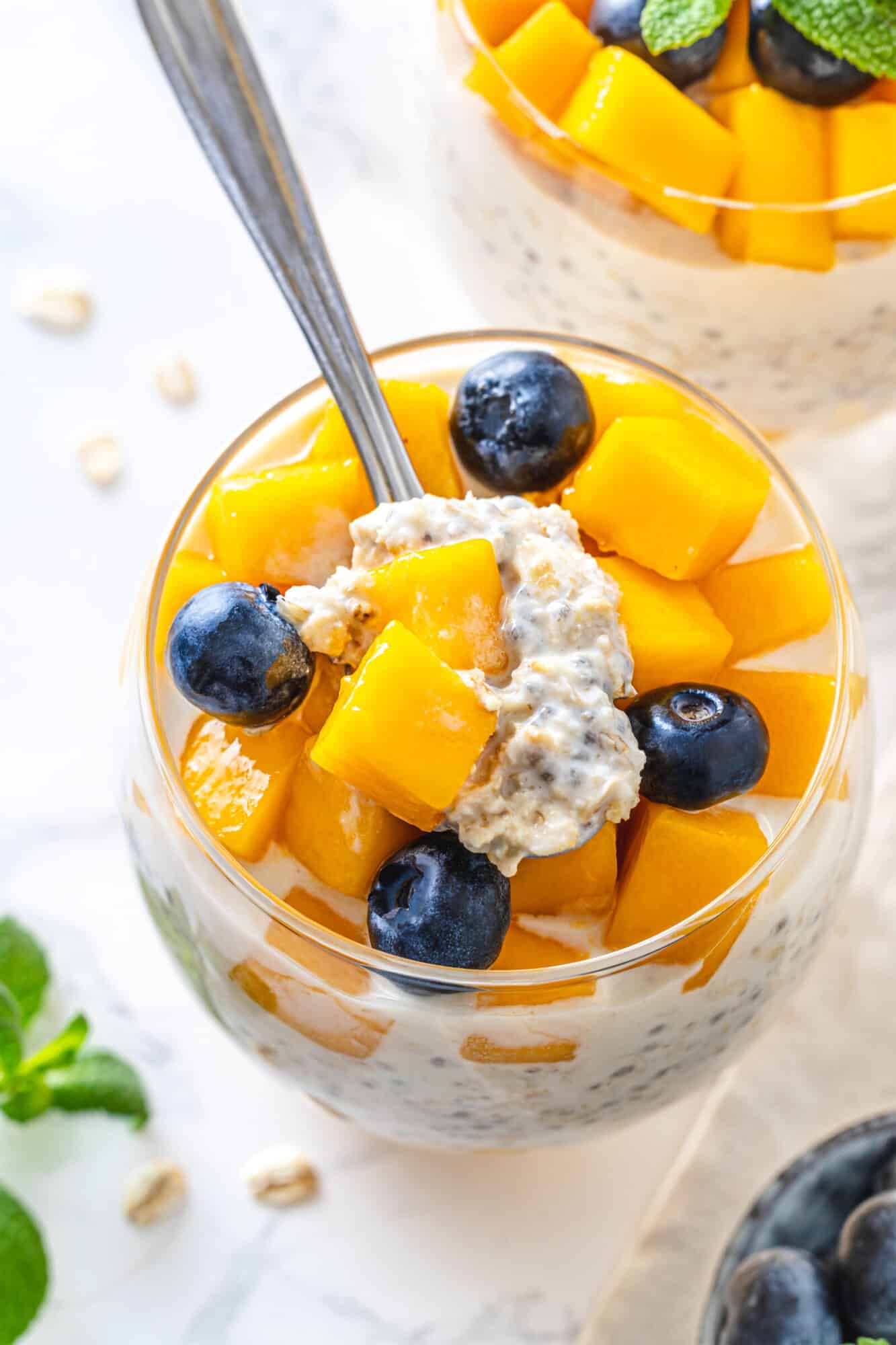 Overnight oats and mango with blueberries served with a spoon.