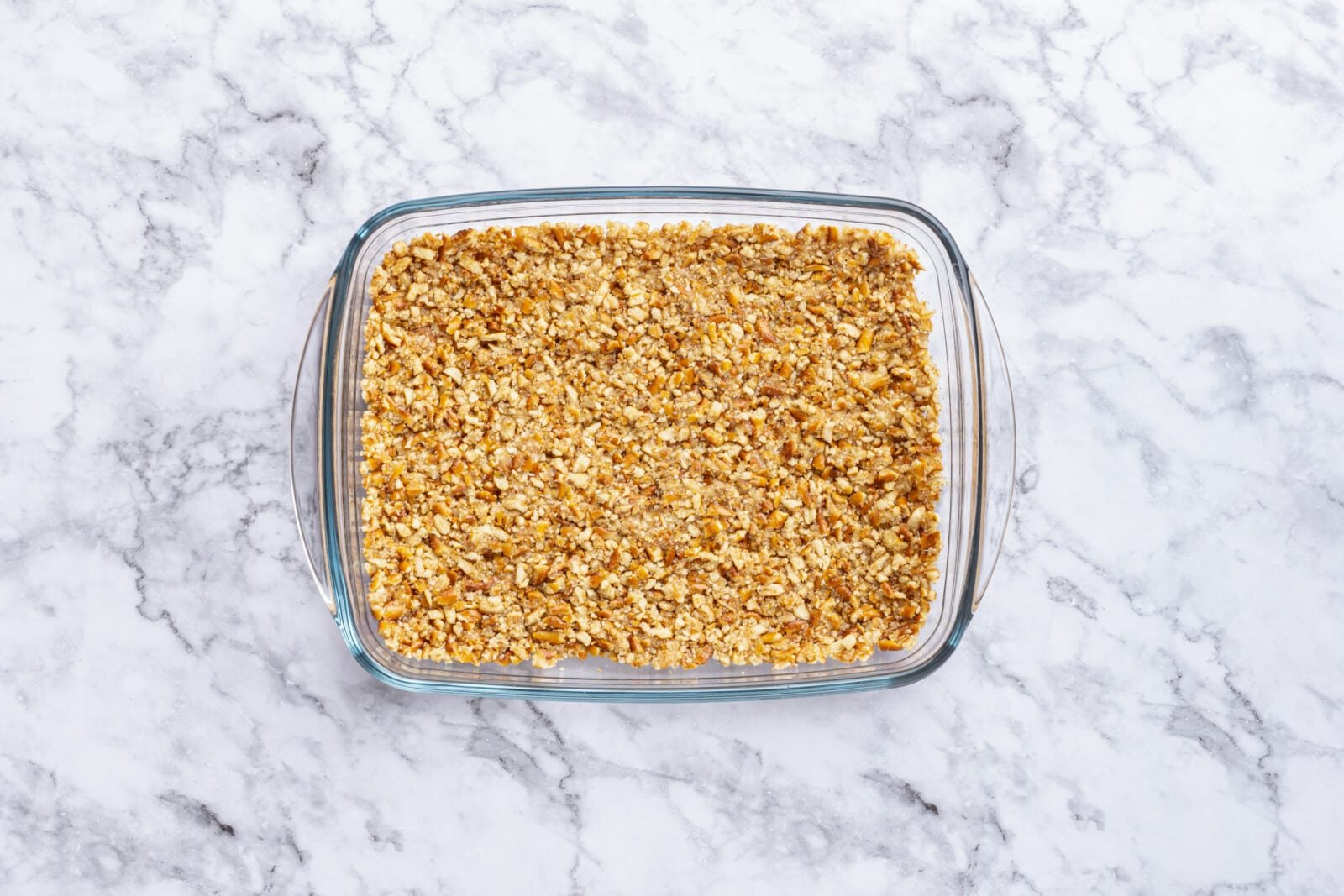 Step-by-Step Strawberry Jello Pretzel Salad Pretzel, butter, and sugar mix layered on the bottom of a baking dish.