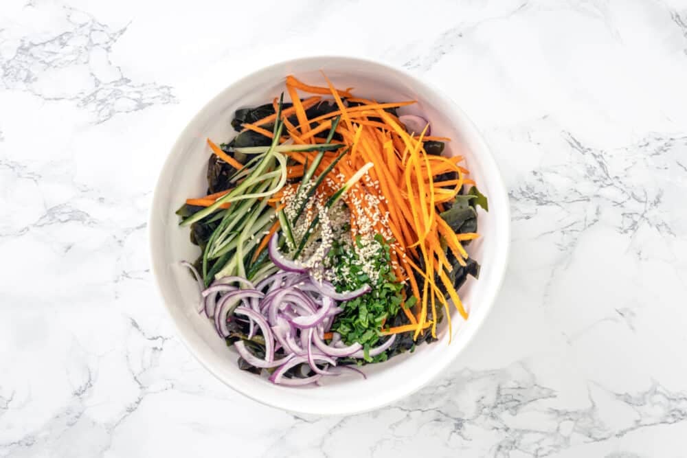 Red onion, cucumber, and carrot all julienned added into the bowl with wakame with sprinkled cilantro and sesame seeds on top.