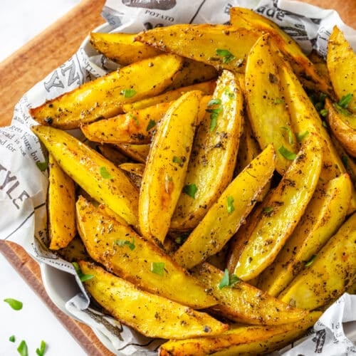 Roasted potato wedges in a bowl served with paper, topped with parsley garnish.
