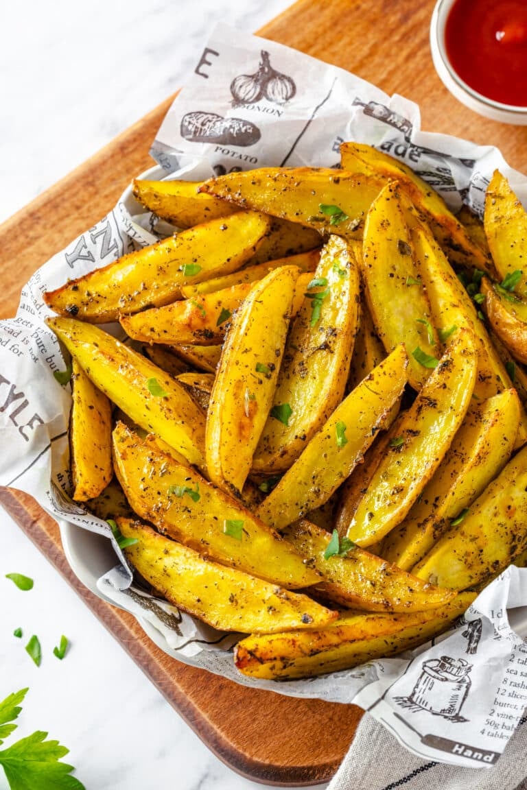Roasted potato wedges in a bowl served with paper, topped with parsley garnish.