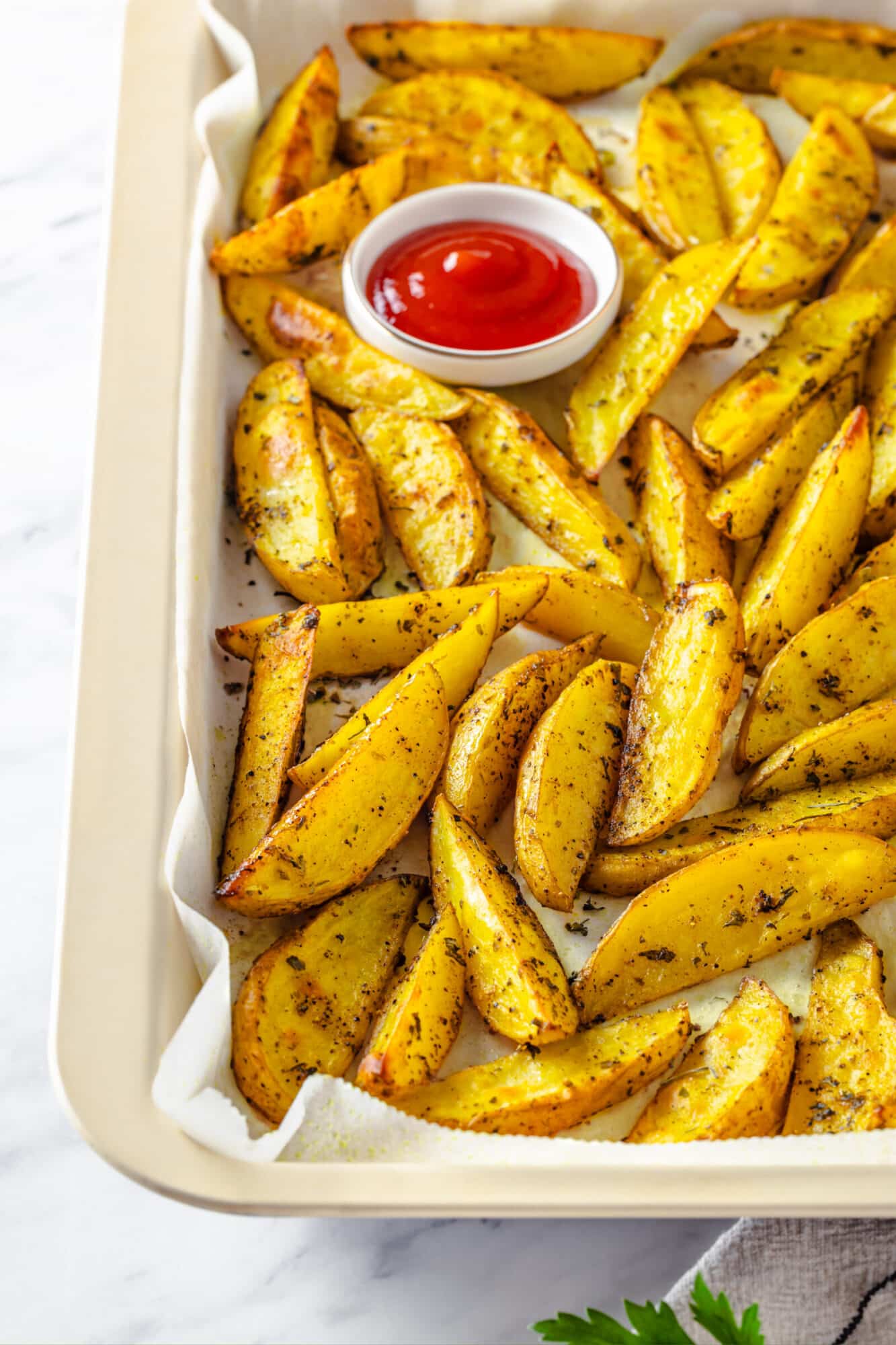 Roasted potato wedges in a pan with ketchup on the side in a bowl to dip.