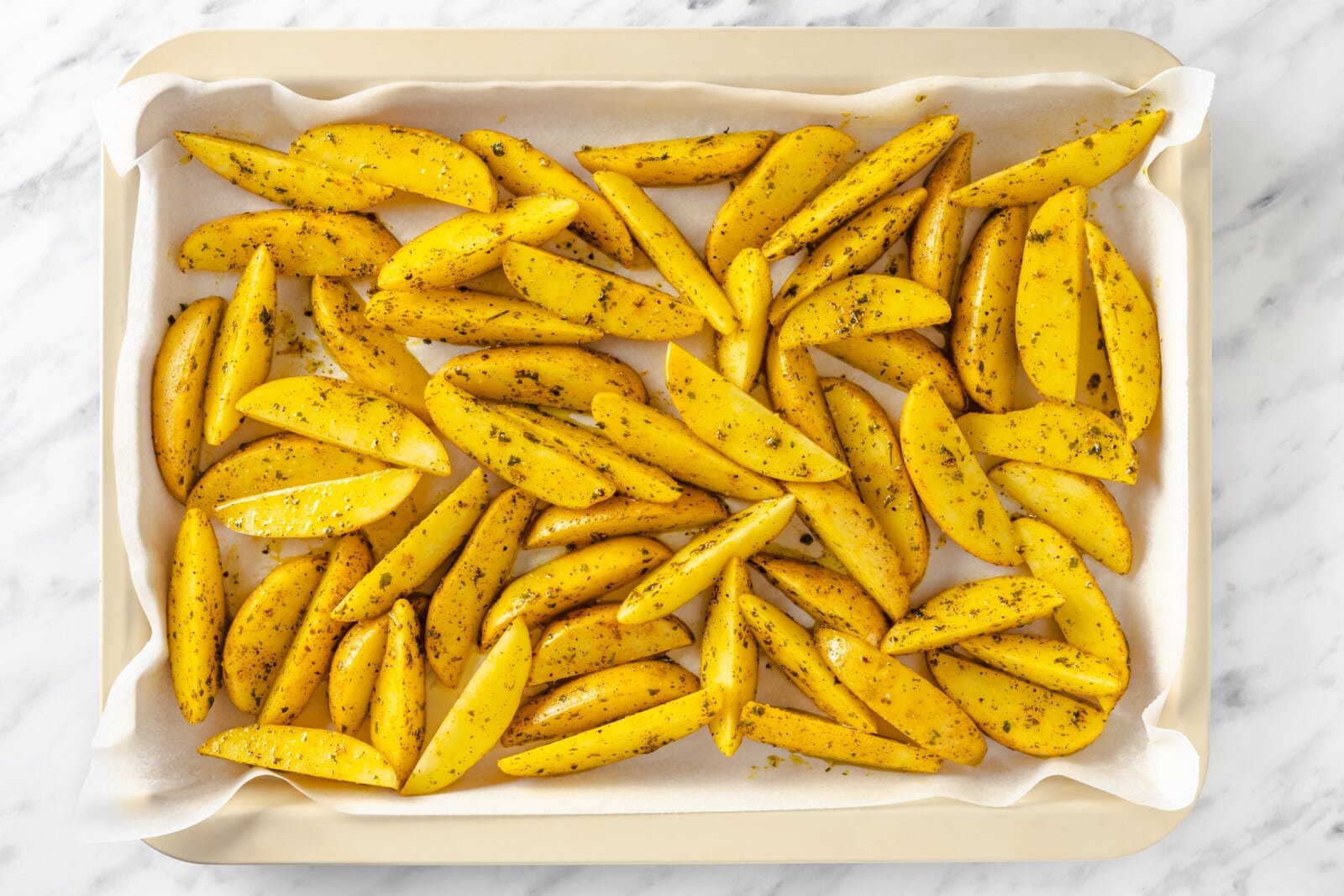 Seasoned potato wedges in a pan with parchment paper.