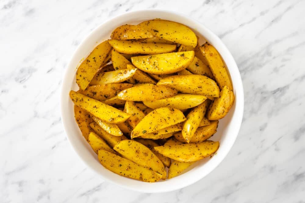 Seasoned potato wedges in a white bowl.