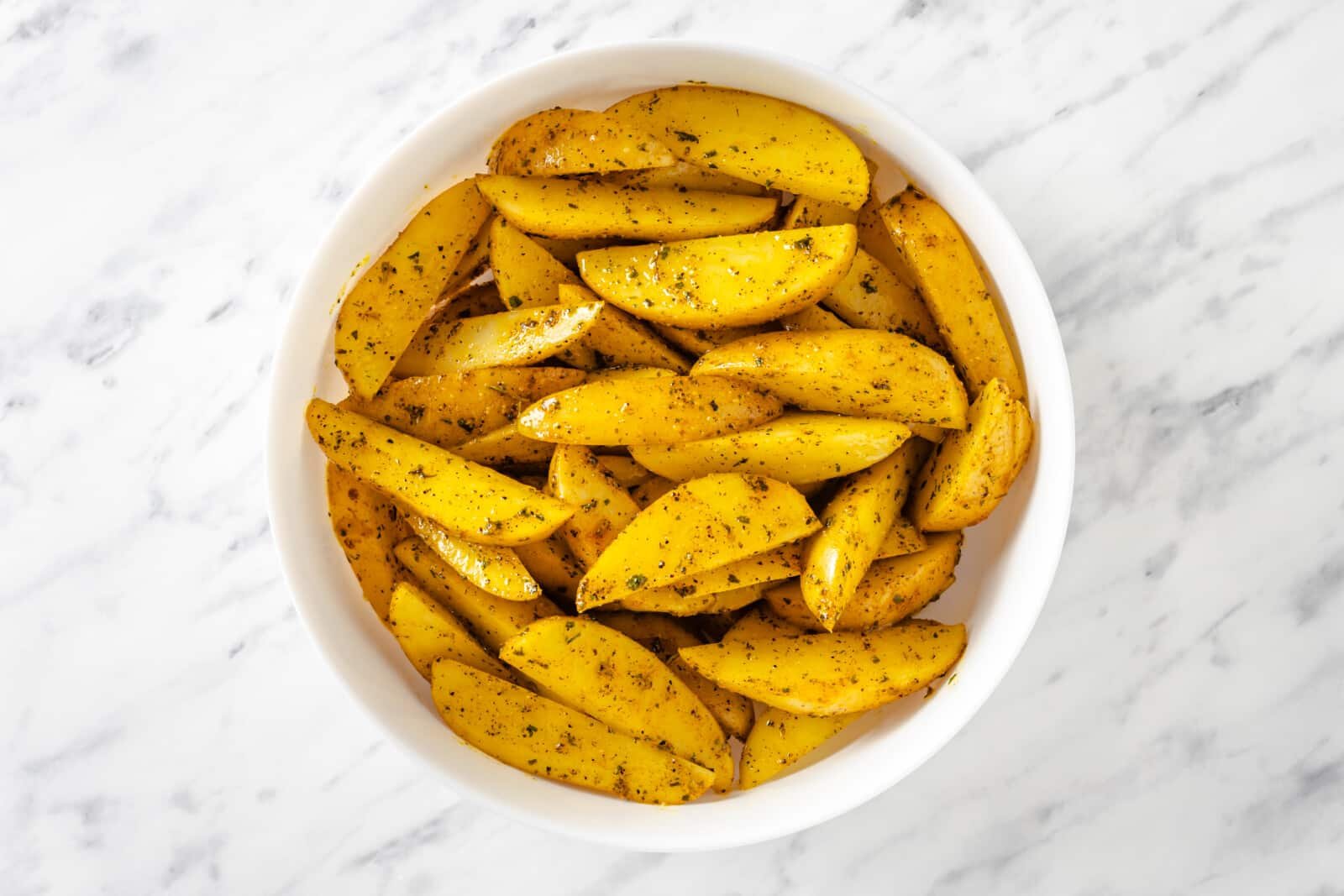 Seasoned potato wedges in a white bowl.