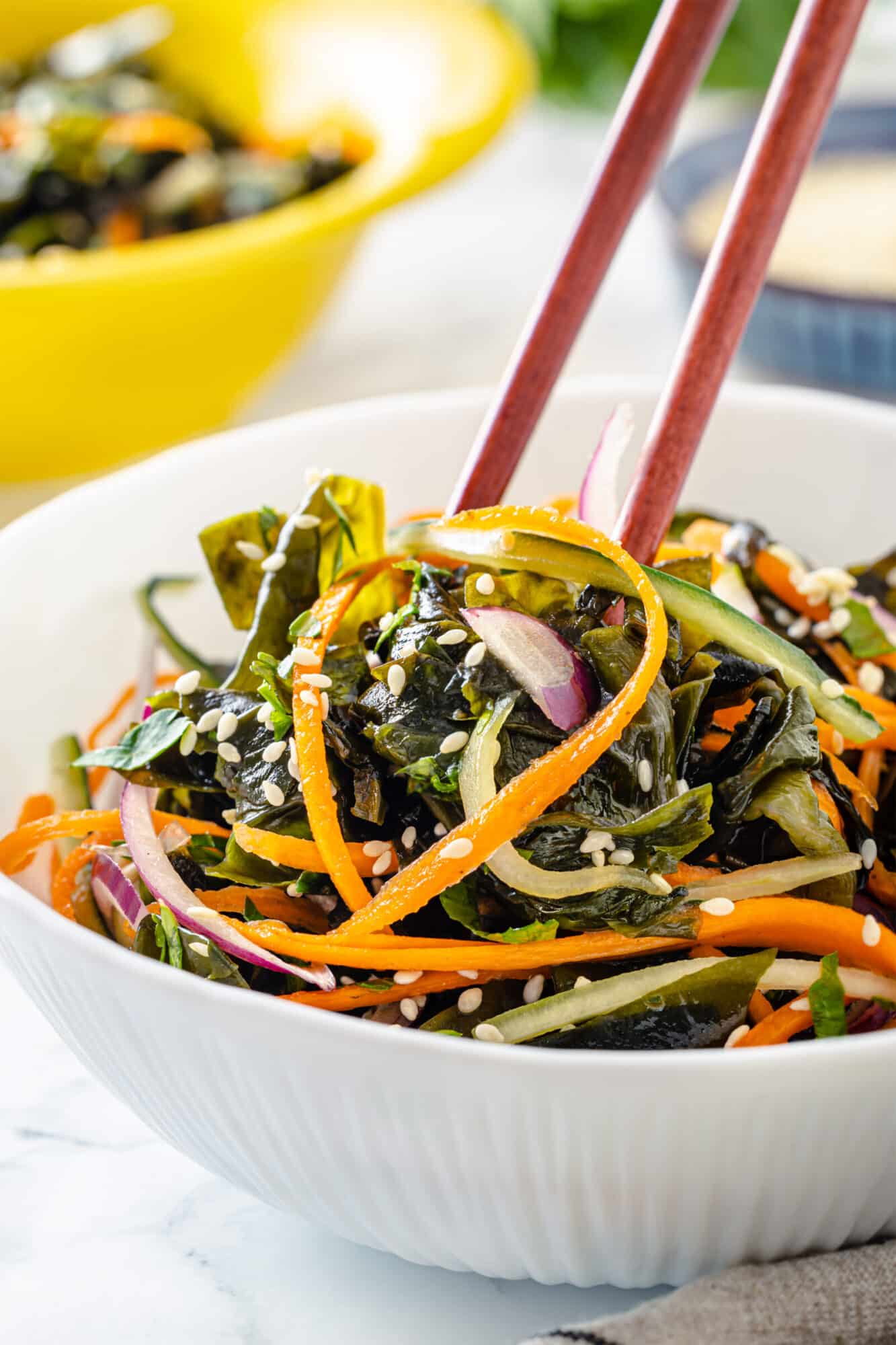 Seaweed salad in a white bowl with chopsticks.