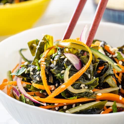 Seaweed salad in a white bowl with chopsticks.