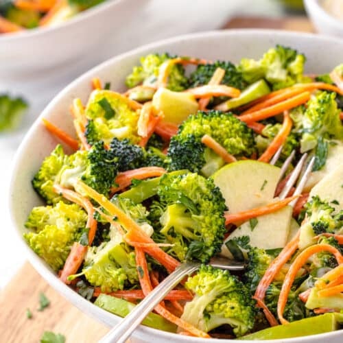 Serving broccoli and apple salad in a white bowl with a fork on the side.