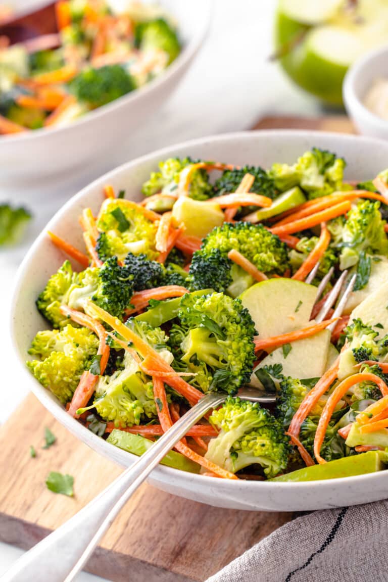 Serving broccoli and apple salad in a white bowl with a fork on the side.