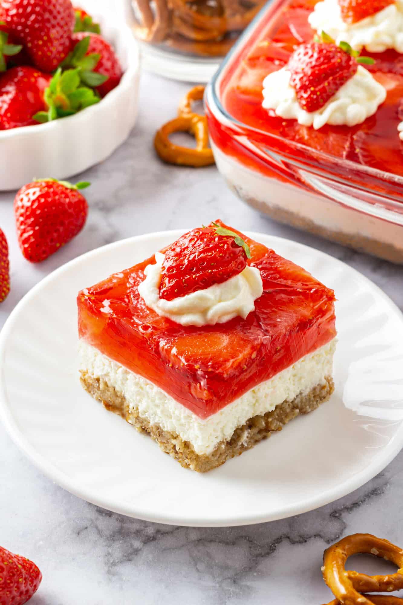 Step-by-Step Strawberry Jello Pretzel Salad Strawberry Jello Pretzel Salad square atop a plate with sliced strawberries on top.
